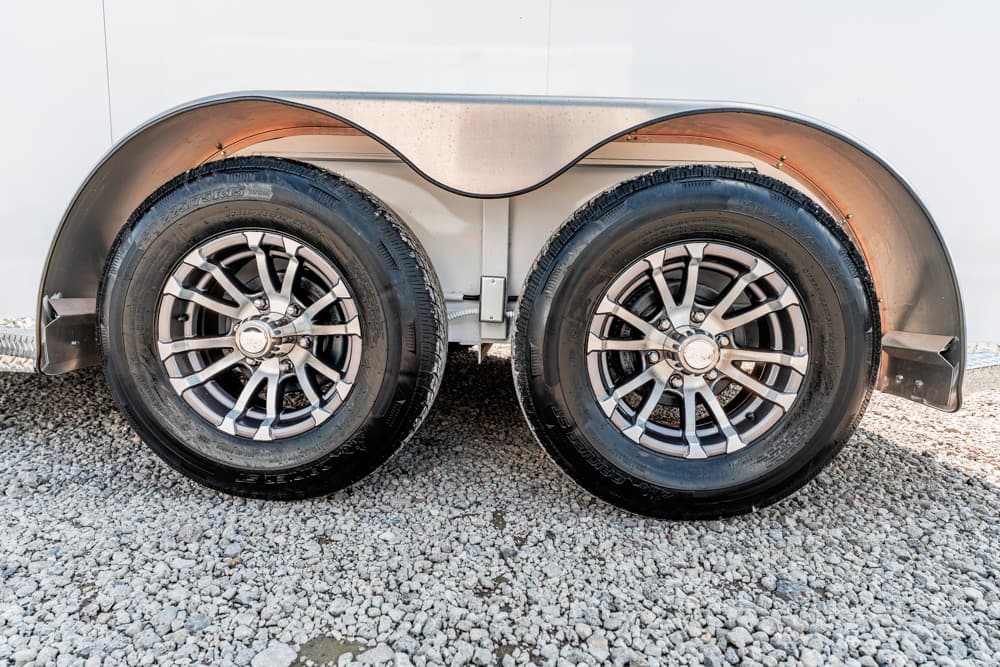 Dual-axle trailer wheels with chrome rims under curved metal fenders on a gravel surface