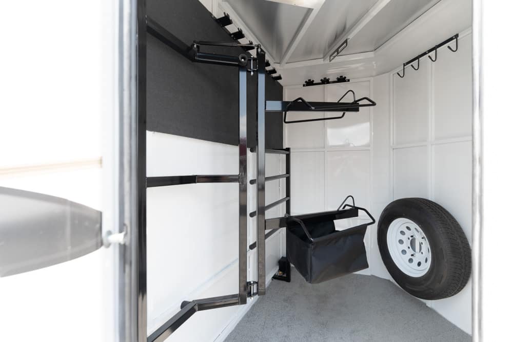 Interior of a cargo trailer with wall-mounted storage racks, hooks, and a spare tire on the right edge.