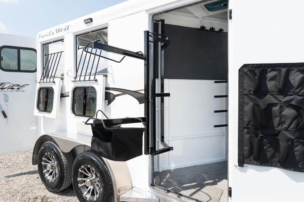 White horse trailer with open side door revealing tack area, hanging racks and saddle bag attachment.