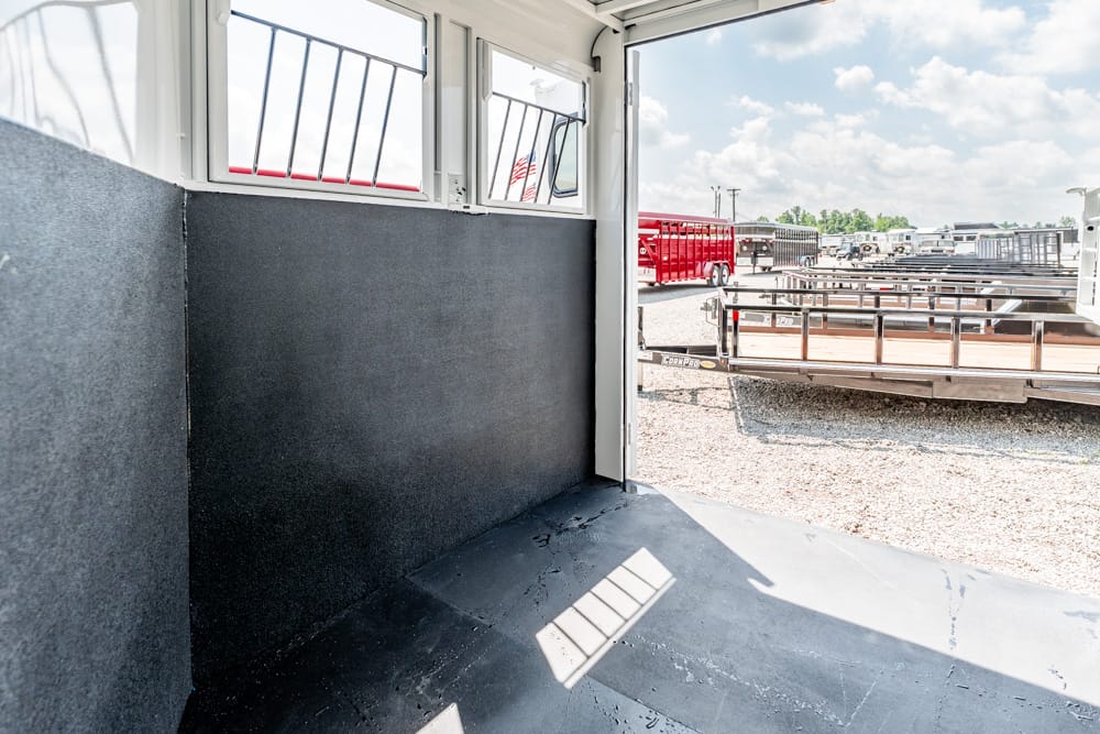 Interior of a trailer with dark padded walls, open side door, and a sunny trailer yard outside with multiple trailers in view.