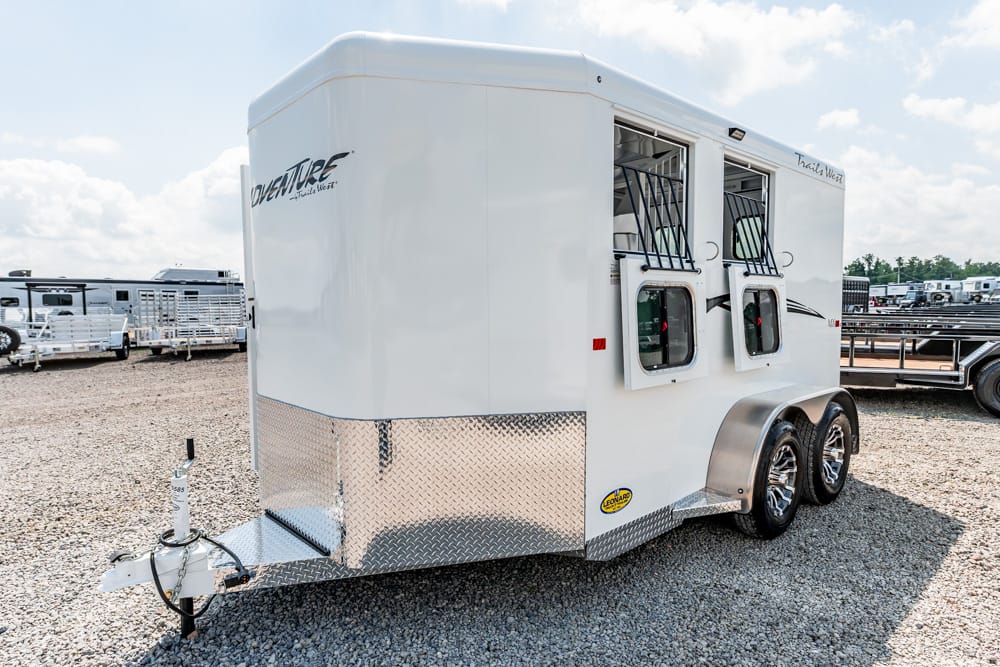 White gooseneck horse trailer with two side loading windows, diamond-plate front, and tandem axles on a gravel lot.