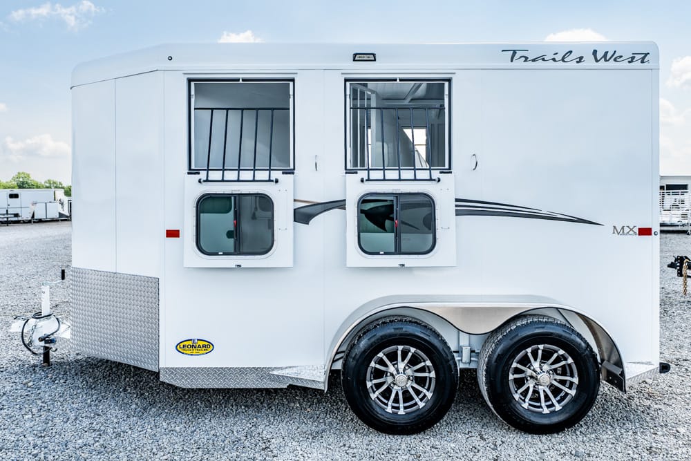 White Trails West horse trailer with two barred windows and tandem wheels on gravel.