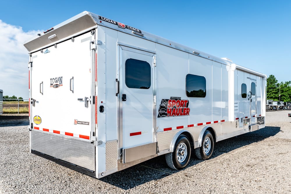 Large white sport hauler trailer with chrome trim and two axles, parked on a gravel lot under a blue sky