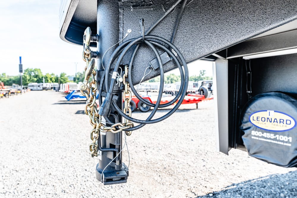 Close-up of a trailer hitch with coiled cables and hanging chains, spare tire cover on the side.
