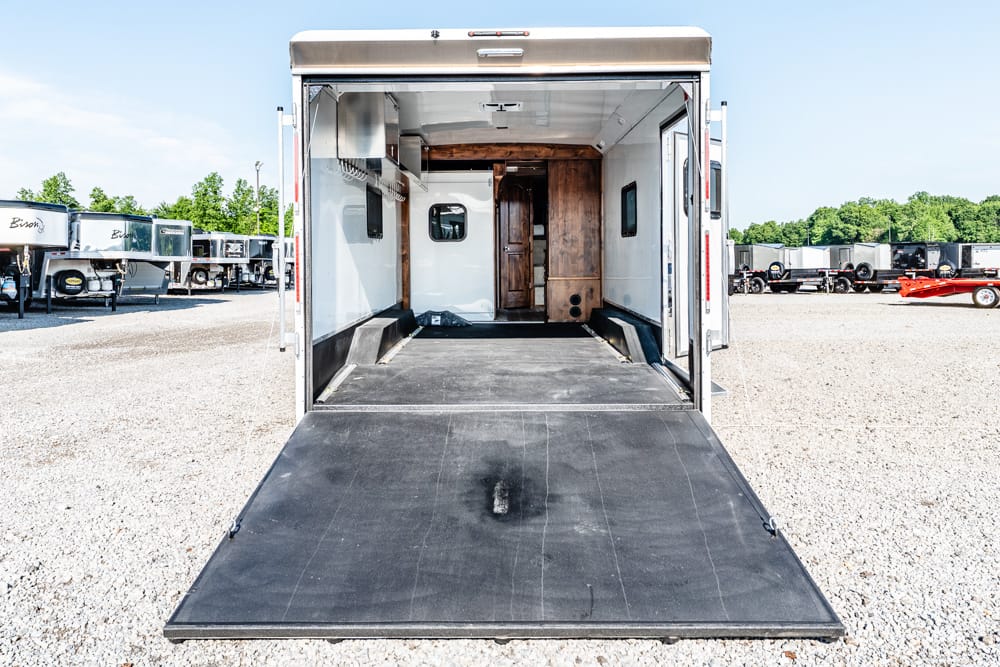 Open cargo trailer with a lowered ramp, exposing a spacious interior and wooden cabinet at the far end