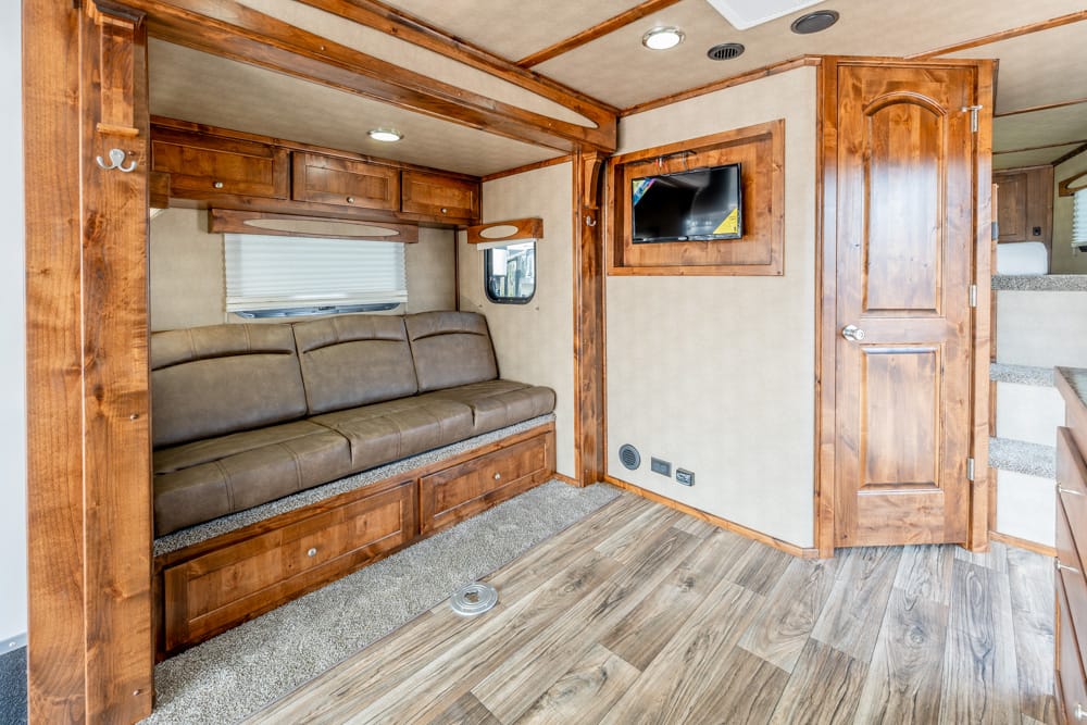 Wood-paneled RV living area with a brown upholstered sofa, overhead cabinets, and a window with blinds.