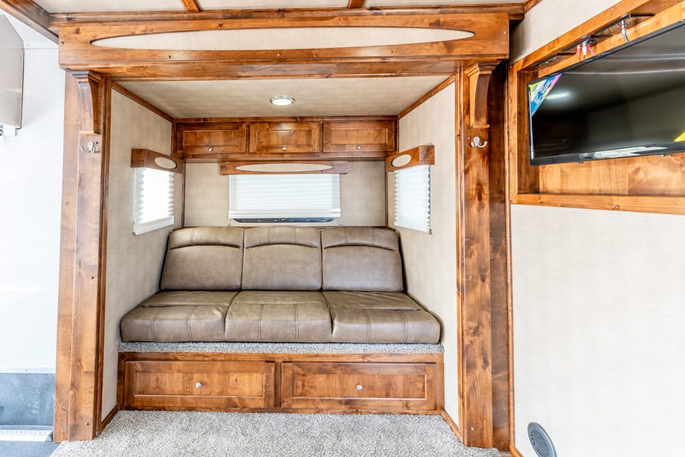 Wood-paneled RV living area with a brown leather sofa, built-in storage drawers beneath, and small windows with blinds.