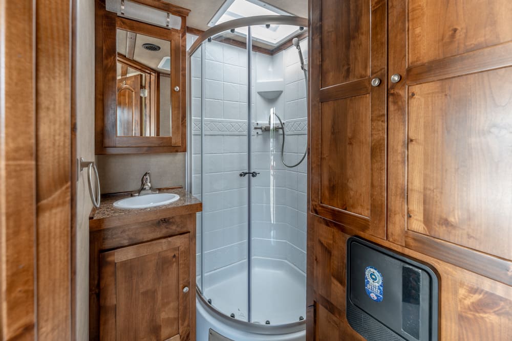 Wooden bathroom with a curved glass shower enclosure, sink and mirror cabinet, warm brown cabinetry, and a compact vanity.