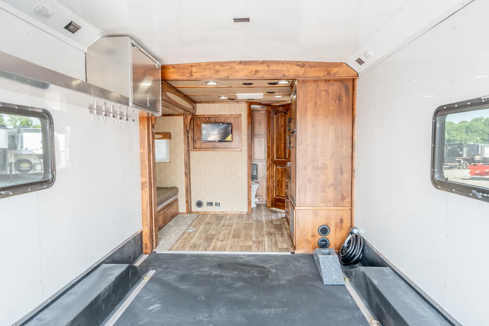 Interior of a wood-paneled RV/travel trailer: rear cargo area opens to living space with built-in cabinets, a small wall TV, seating nook, and wood flooring.