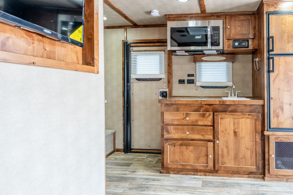 Wood-paneled RV kitchen with microwave above a counter, sink, and three drawers; refrigerator on the right.