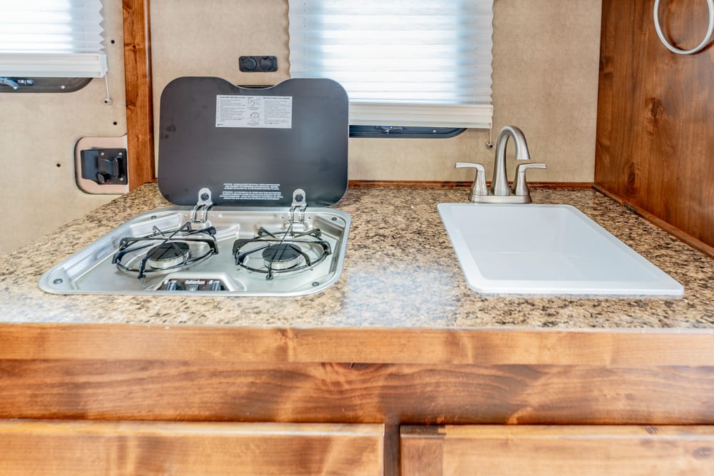 RV kitchenette with a two-burner gas stove and a white rectangular sink on a speckled countertop.