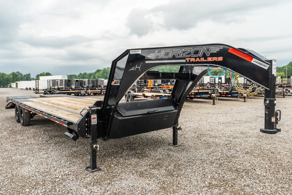 Black Horizon trailers gooseneck flatbed trailer with a wooden deck, parked in a gravel lot with other trailers in the background