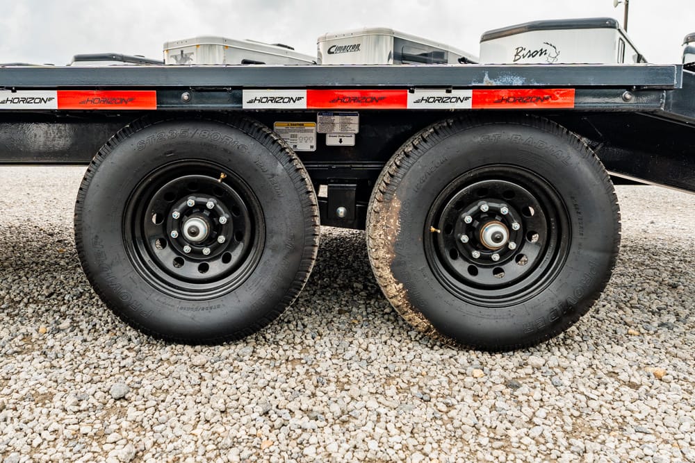 Dual trailer wheels on a flatbed trailer parked on gravel, with red Horizon reflectors along the side.