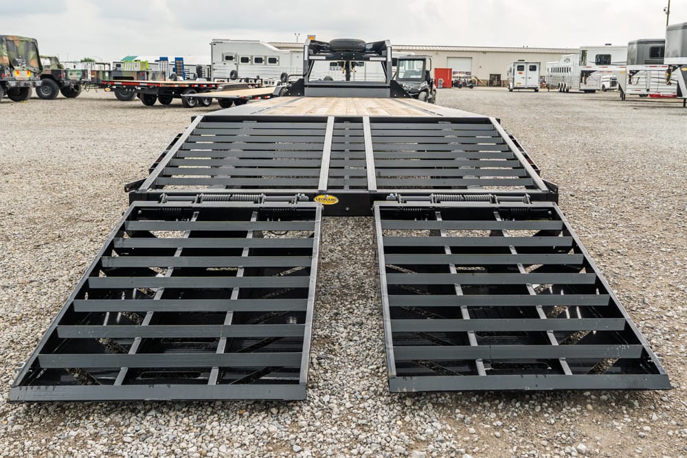 Industrial trailer ramps extended on a gravel lot, ready for loading large equipment or vehicles, with a flatbed behind them