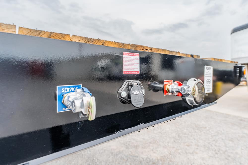 Close-up of a black trailer tongue with service and emergency valves, including a blue 'SERVICE' label and a Phillips lock.