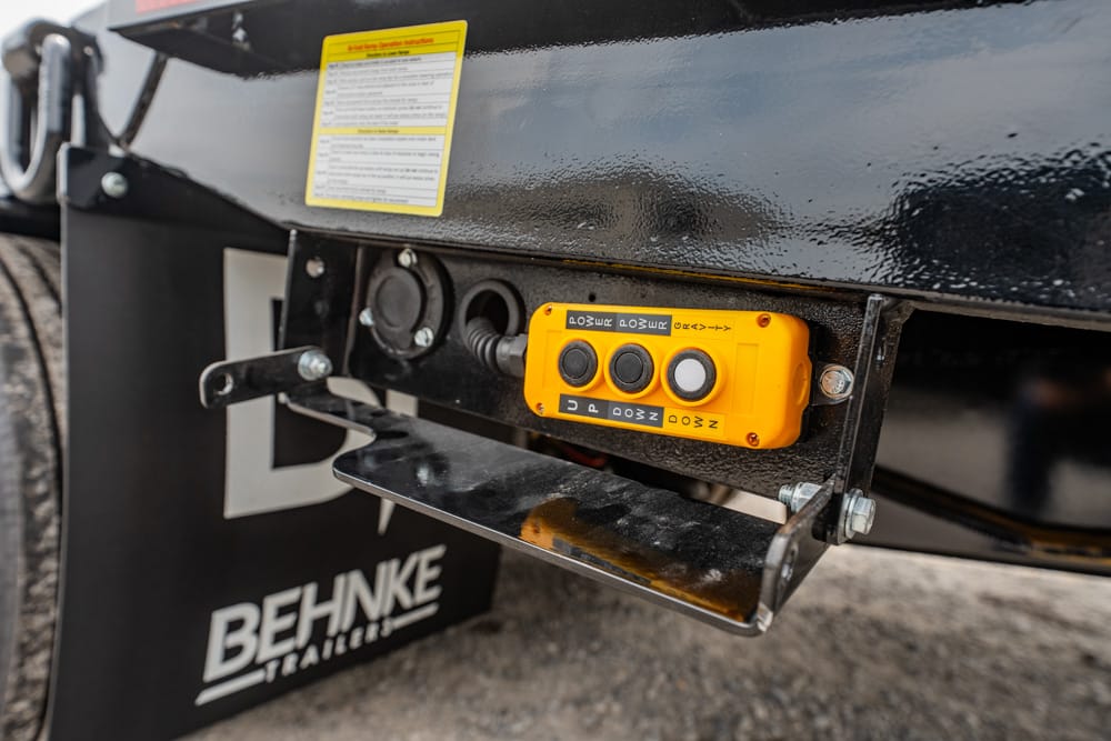 Orange trailer brake controller mounted on a black trailer frame with four black buttons and labeled switches.