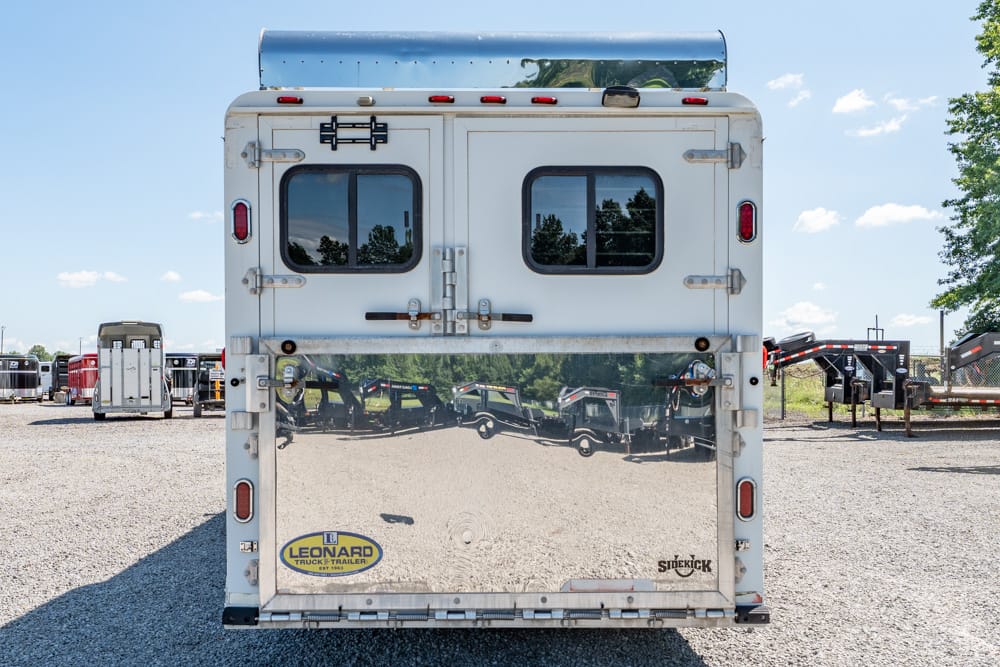 Rear view of a silver trailer on a gravel lot, featuring two small rectangular windows and a reflective lower panel.