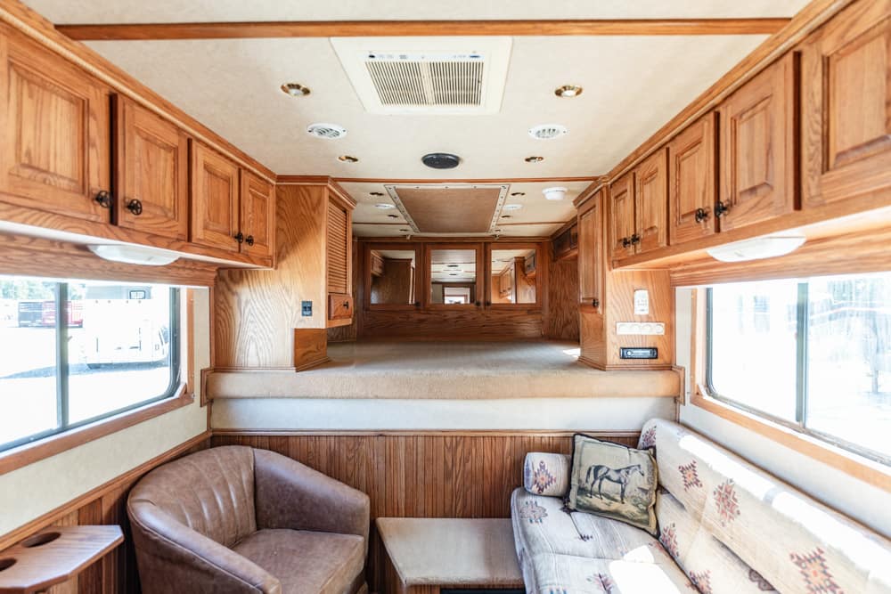 Wood-paneled RV living area with built-in cabinets, a sofa with decorative pillows, and a brown chair by a window