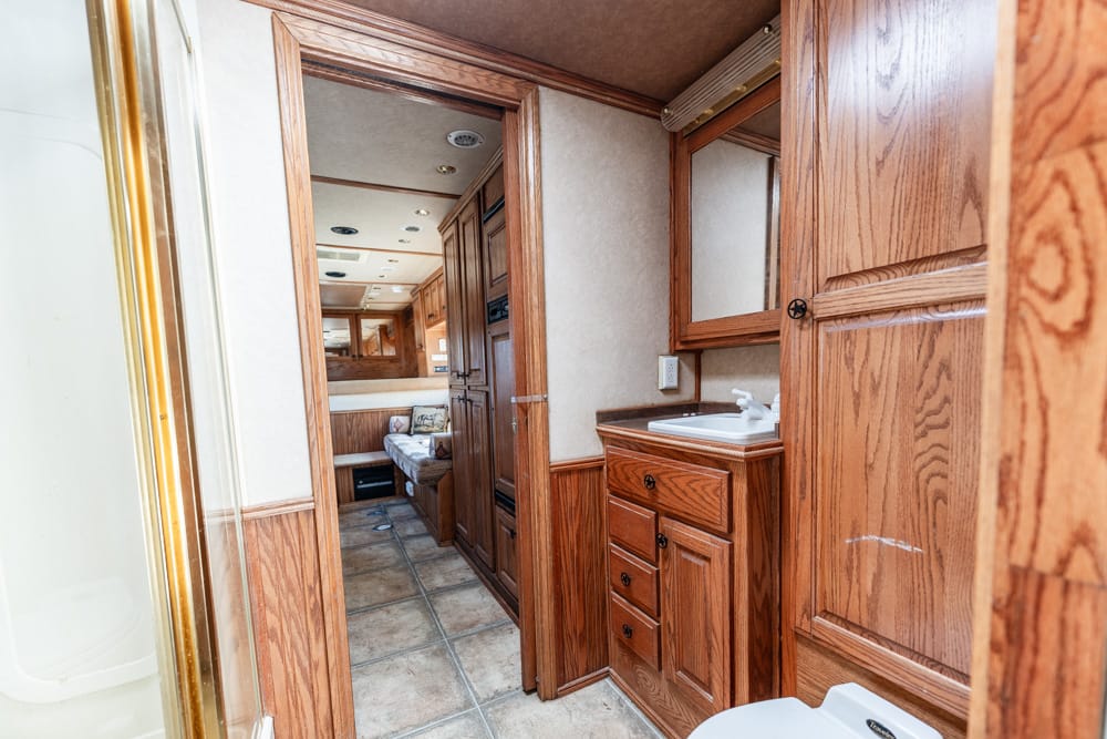 Interior of an RV bathroom and hallway with wooden cabinets, sink, and mirrored medicine cabinet, conveying a compact living space.