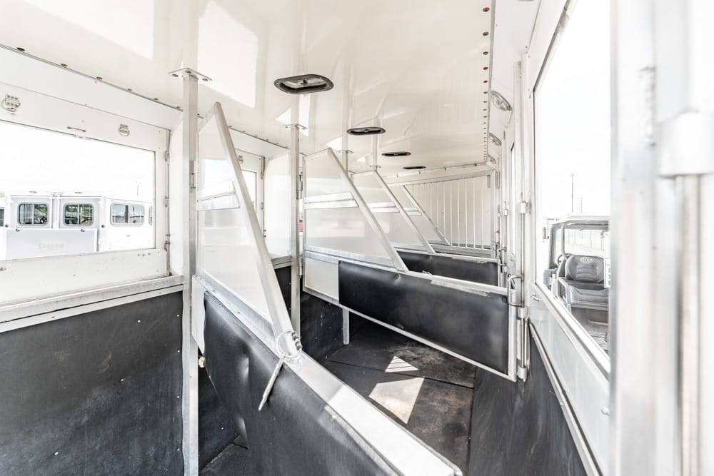 Interior of an empty horse trailer with partitioned stalls and padded walls, ready for loading horses