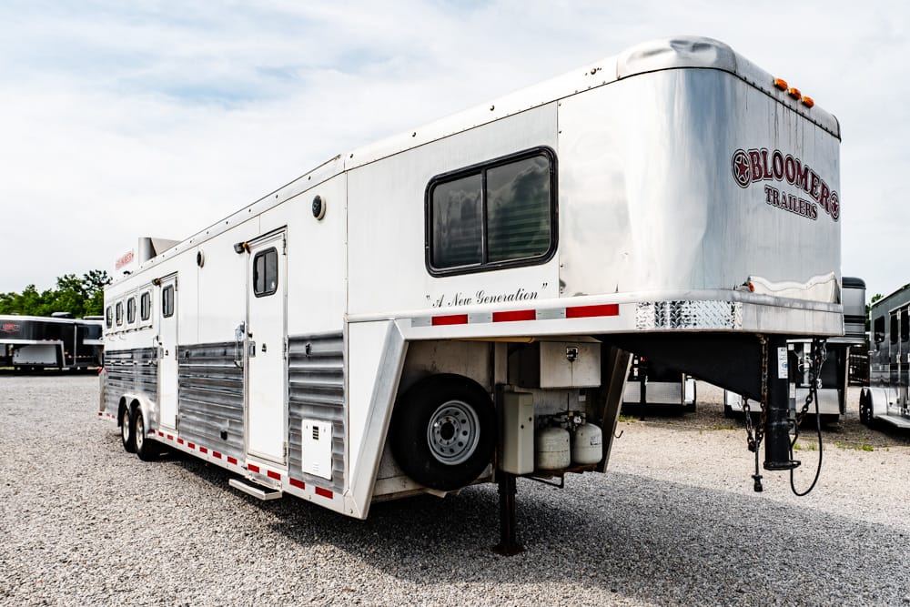 White gooseneck horse trailer with living-quarters, branded 'Bloomer Trailers,' parked on a gravel lot.