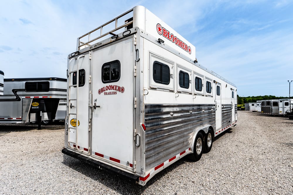White Bloomer's horse trailer with side windows parked on a gravel lot, showing rear and entry doors.
