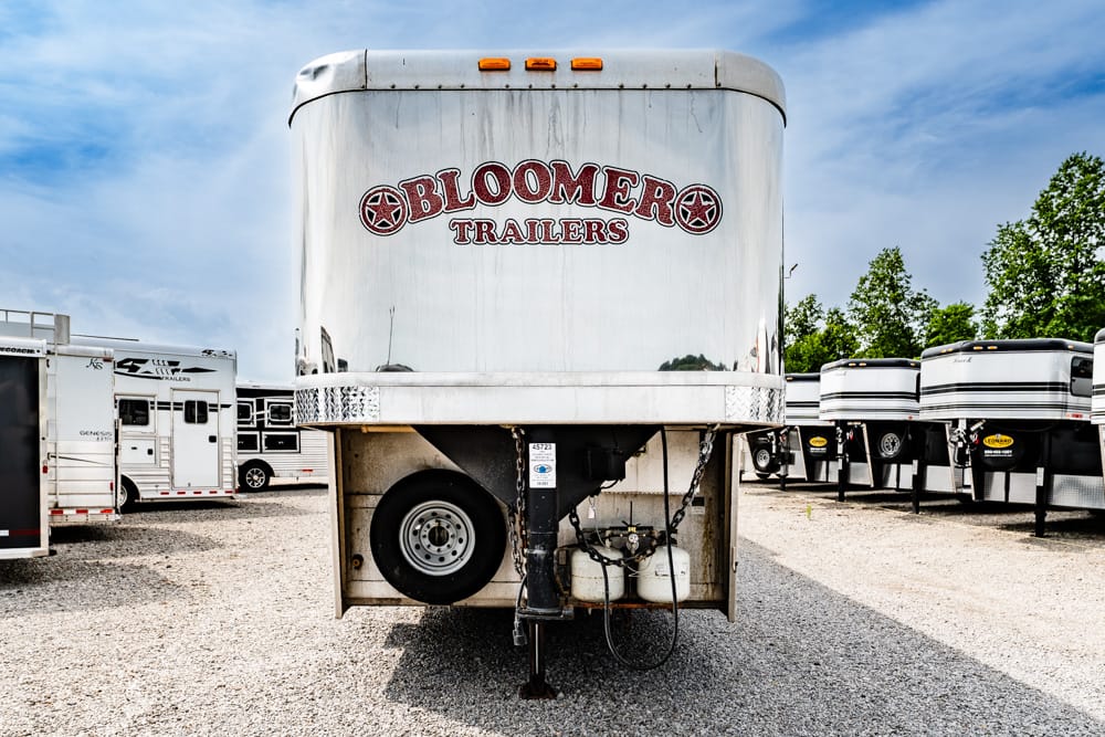Front view of a Bloomer Trailers aluminum trailer in a lot, with spare tire and hitch visible within the front area.