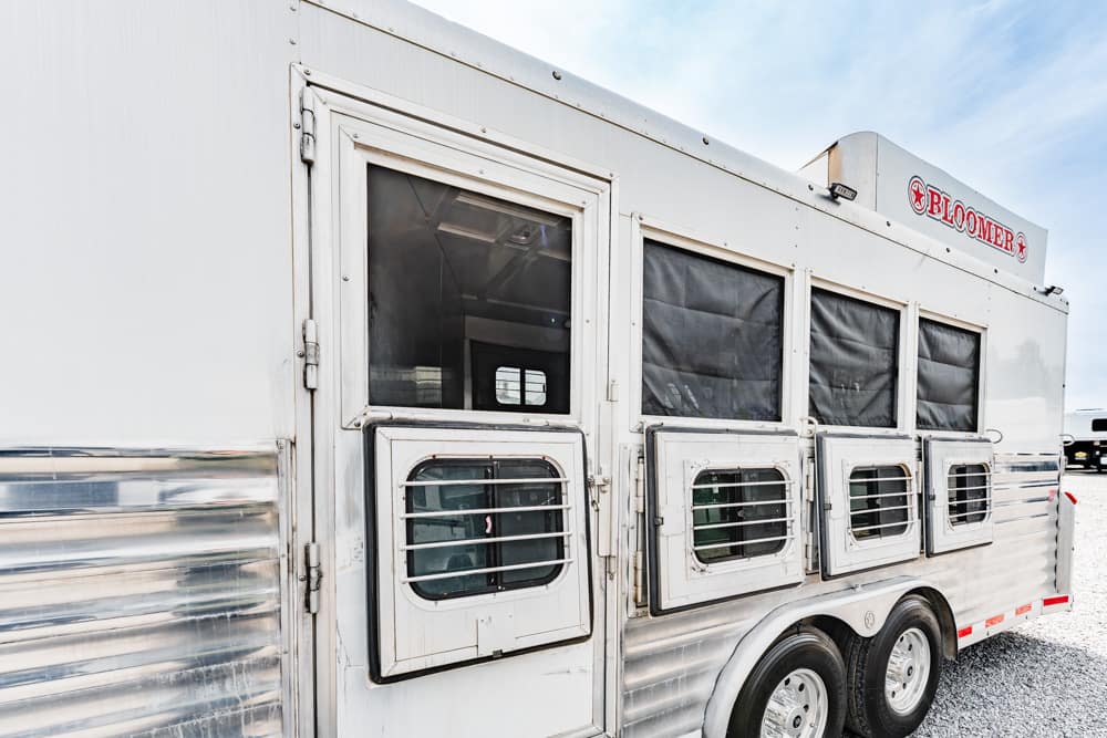 White Bloomer horse trailer with four vented windows parked on a gravel lot.