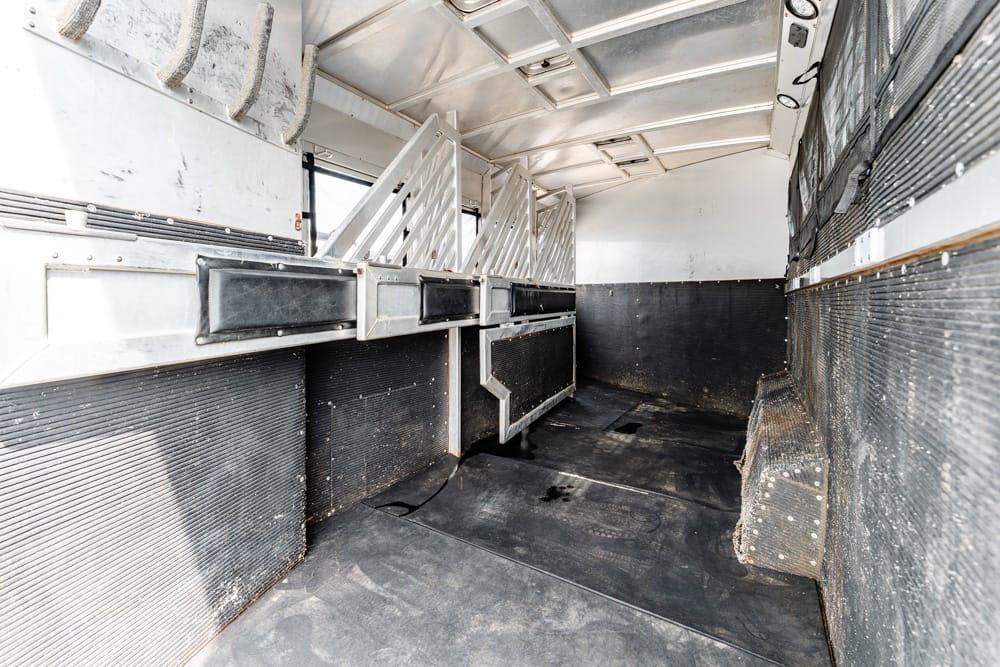 Interior of a metal horse trailer with partitioned stalls and black rubber flooring
