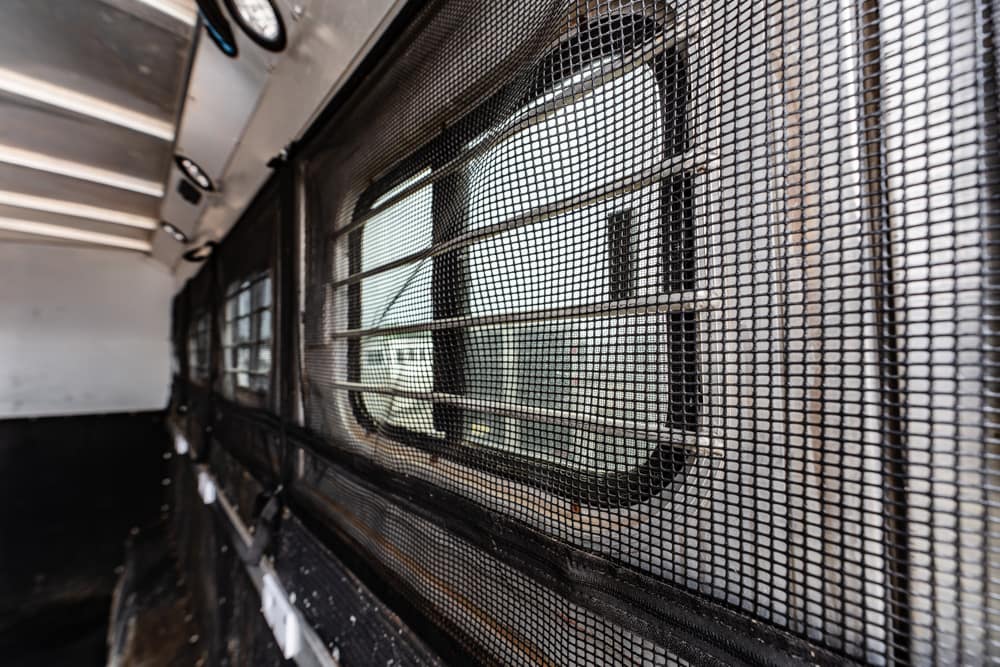 Interior of a vehicle with a metal mesh divider and side window visible through the mesh