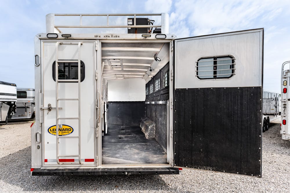 Back of a silver horse trailer with doors wide open, showing an empty aluminum interior and a black rubber floor.