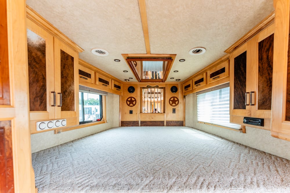 Wood-paneled RV interior with cabinets along both walls, carpeted floor, and large windows on each side