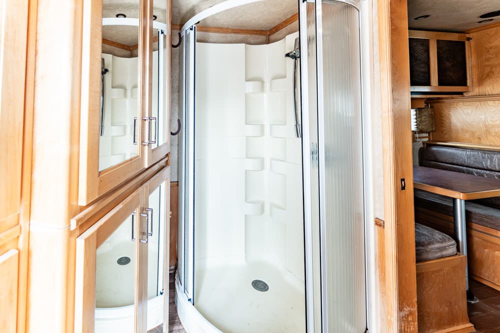RV bathroom with a curved glass shower enclosure, white molded shower walls, and light wood cabinetry surrounding it.