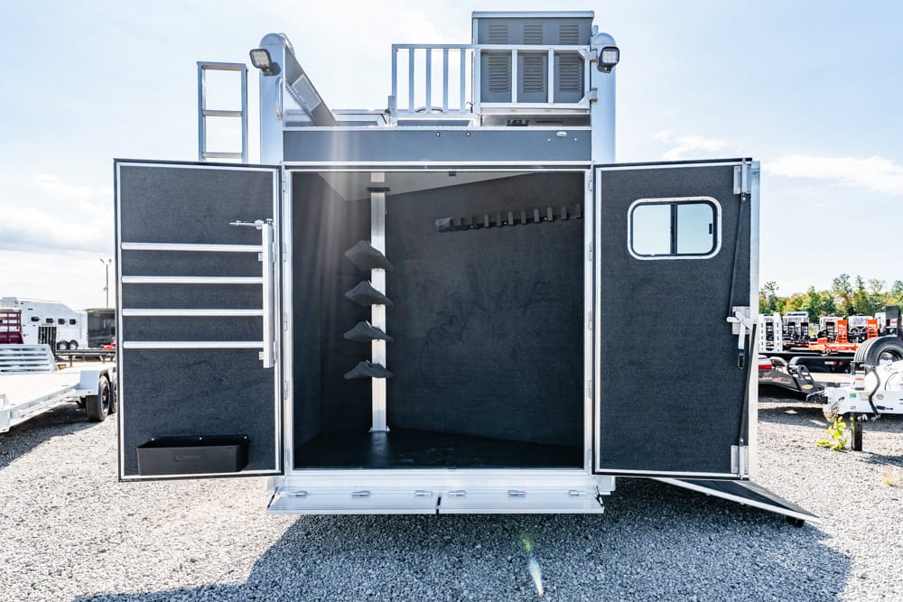 Open back of a black utility trailer with interior racks and hooks, parked on a gravel lot.