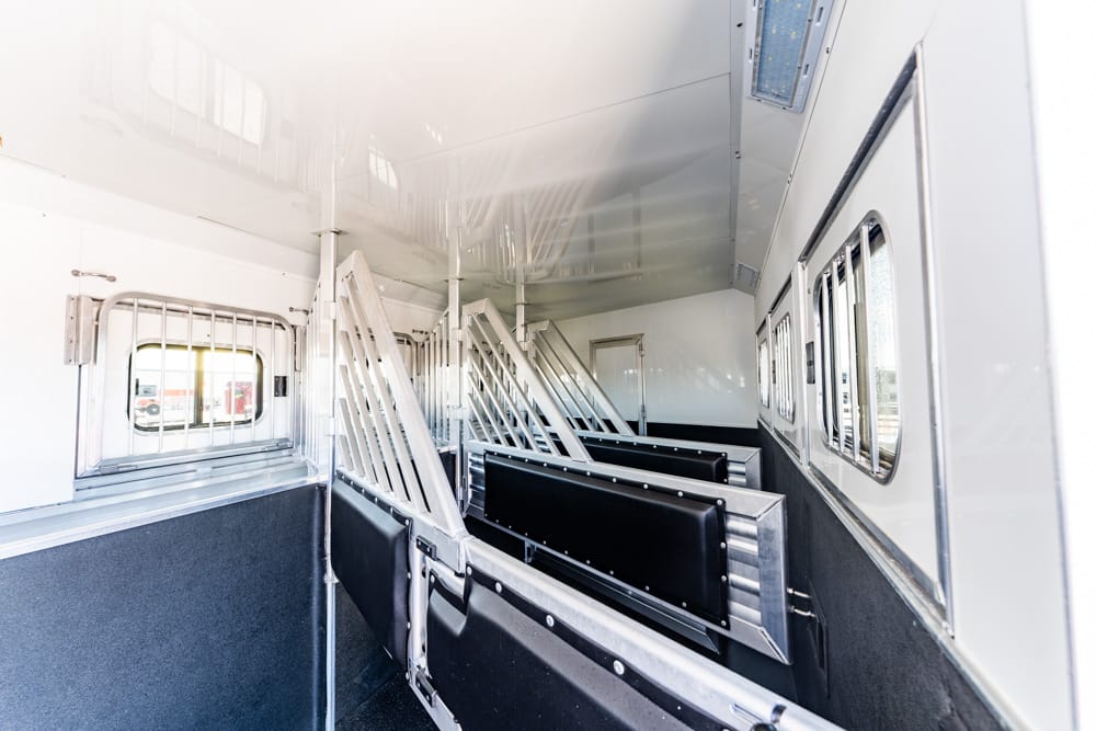 Inside a white transport trailer with metal partitions and black cushioned benches along the wall.