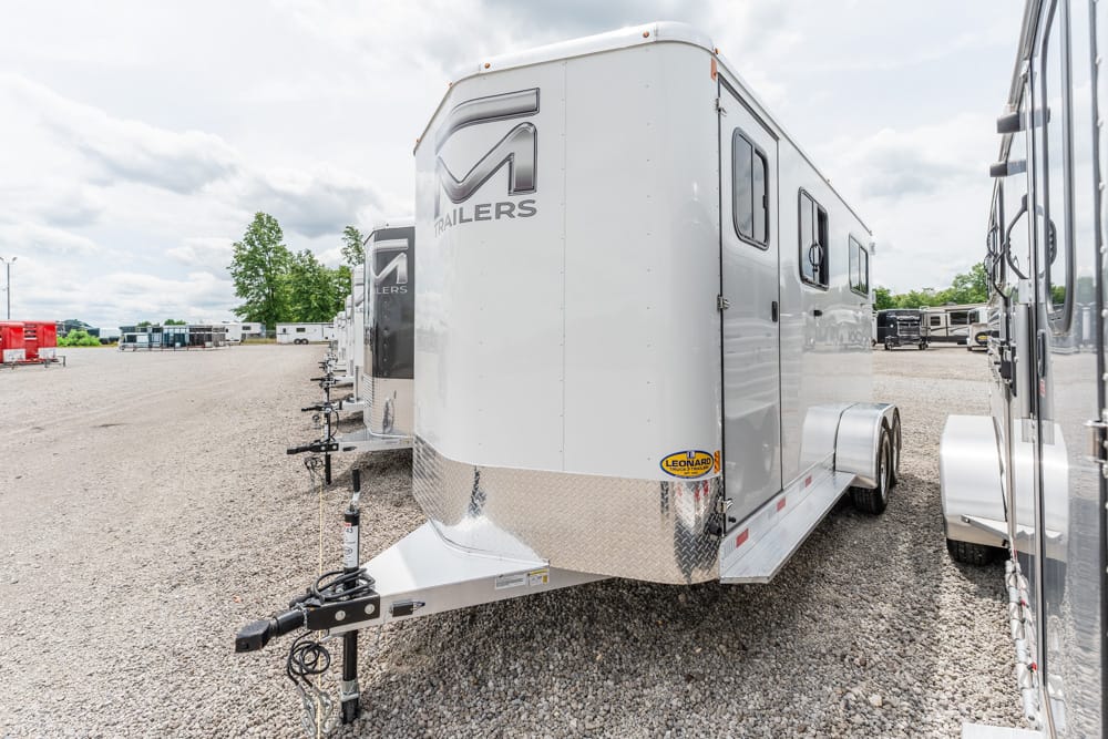 White enclosed trailer with dual axles and a diamond-plate front on a gravel lot at a trailer dealership.