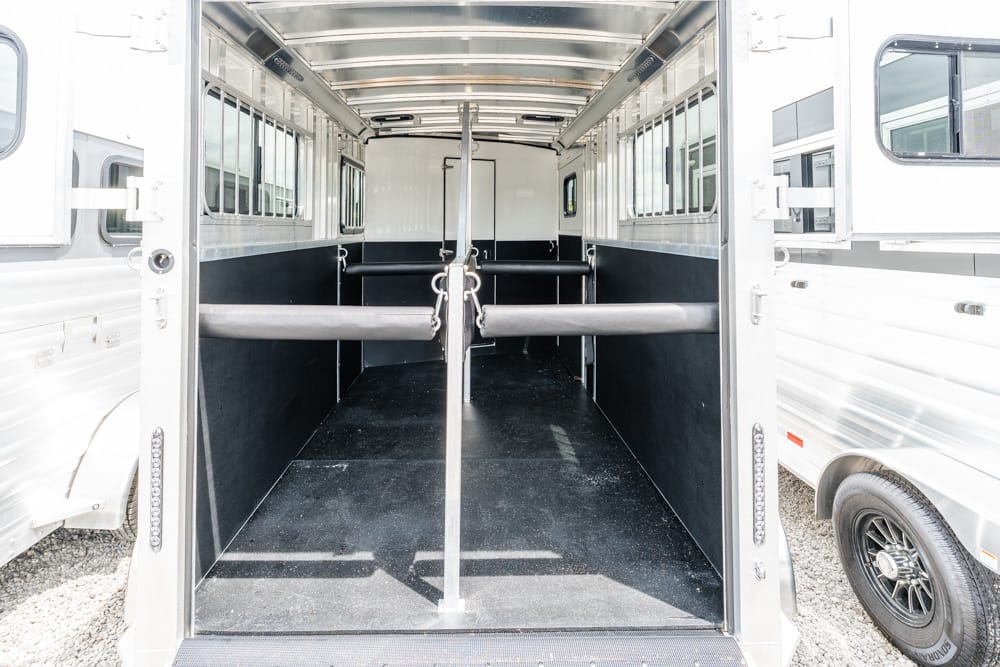 Interior of a two-horse trailer with a center divider and padded walls, empty stalls and daylight at the rear door.