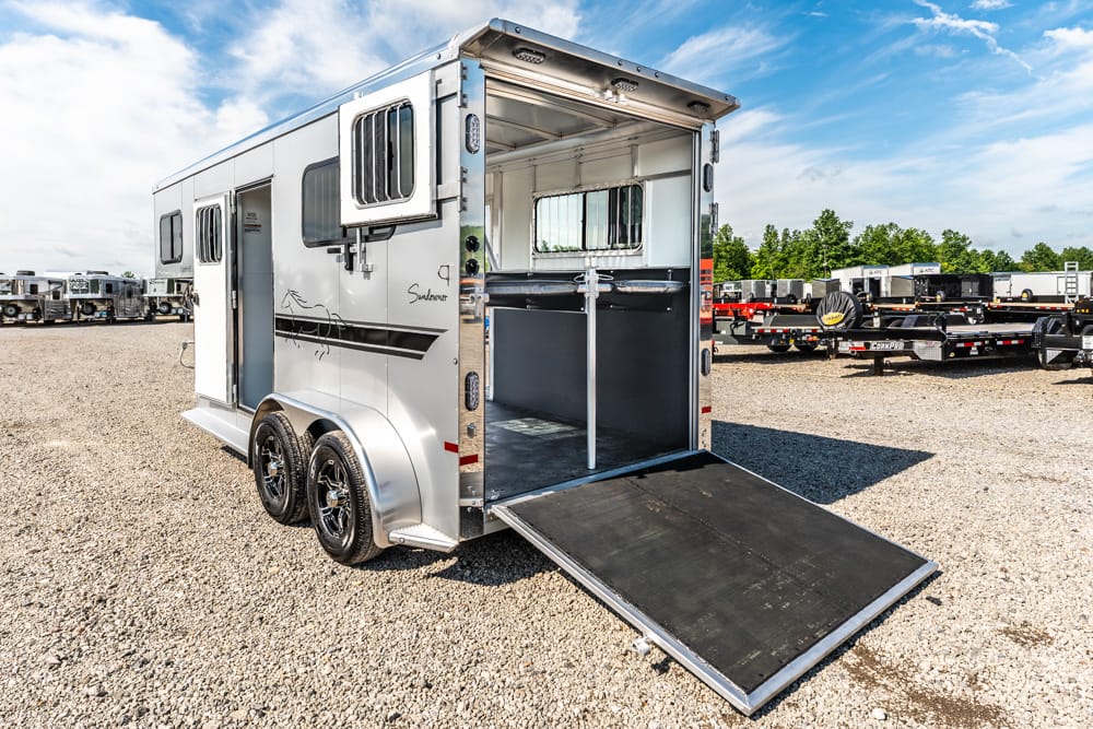 Silver horse trailer with rear ramp lowered for loading, showing interior divider rails and saddle area.
