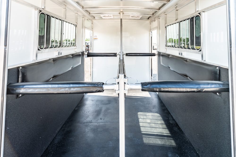 Empty horse trailer interior with two divided stalls, padded black walls and metal rails along the center aisle