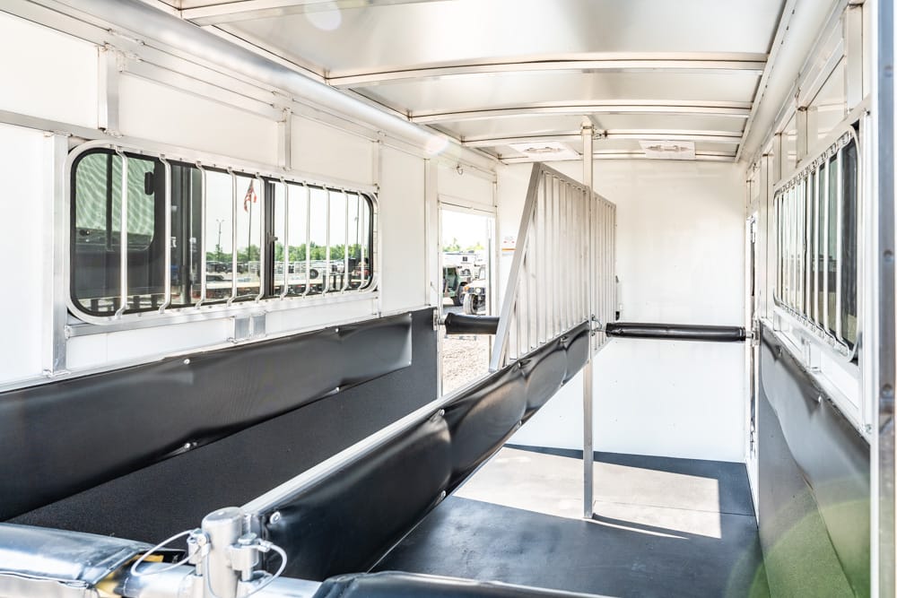 Interior of a white horse trailer with black padded stalls and a vertical divider, empty and ready for horses, windows along the sides.