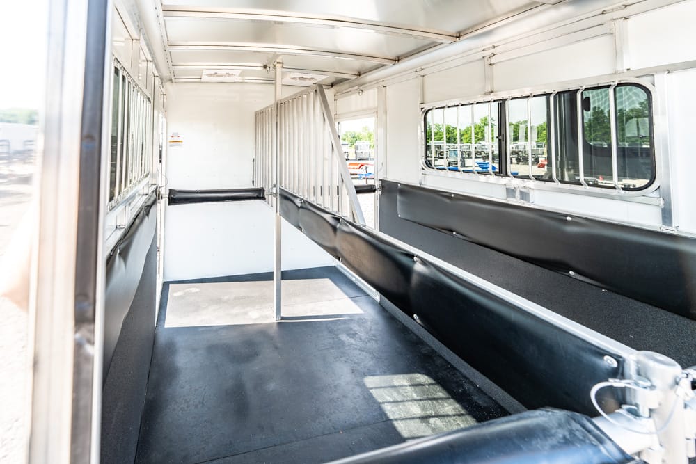 Interior of an empty livestock trailer with metal dividers and black padded walls, reflecting light from side windows.