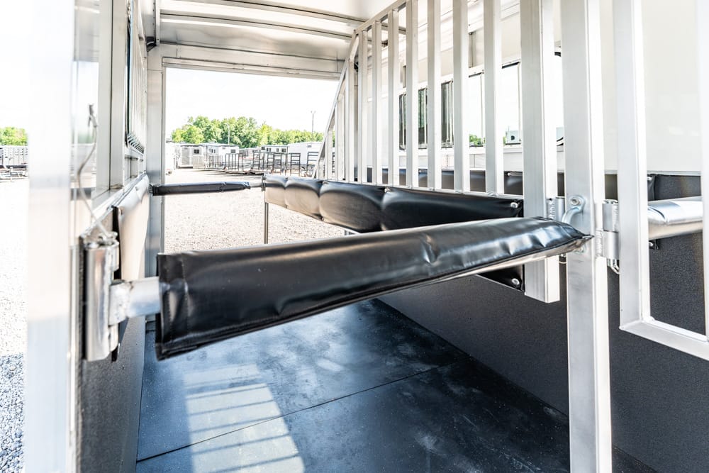 Interior of a metal livestock trailer with padded dividers along the wall, viewed from the doorway.