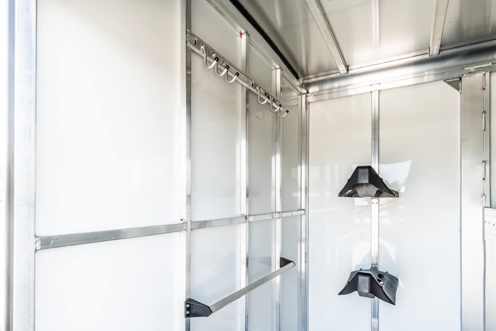 Interior of a silver metal cargo trailer with a row of wall hooks and a vertical rack holding two black holders on the right side