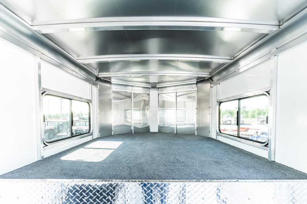 Empty aluminum cargo trailer interior with a carpeted floor and large side windows, seen from the rear ramp.