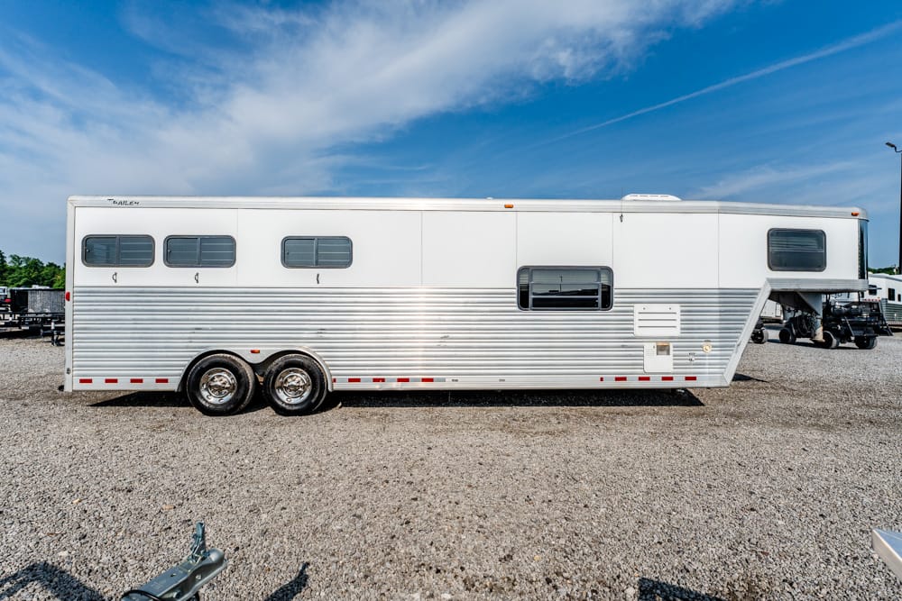 Long silver aluminum travel trailer with multiple windows parked on a gravel lot under a blue sky.