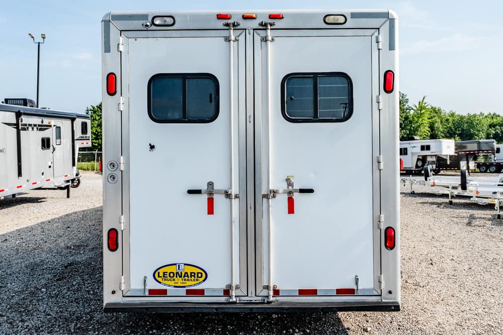Rear view of a white double-door trailer with small windows, red lights, and a Leonard trailer logo at the bottom left.