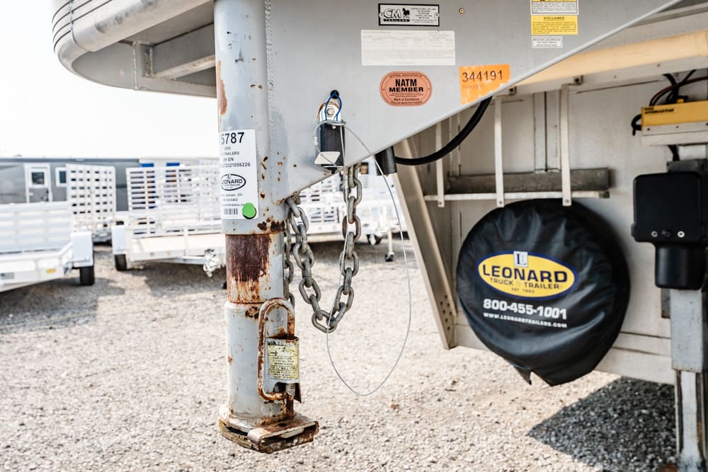 Close-up of a rusted trailer hitch with chains and a padlock on the tongue, Leonard spare tire cover visible in the background