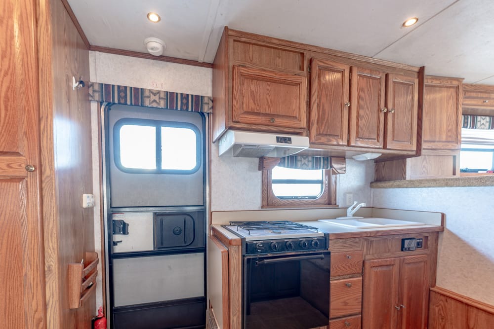 Compact RV kitchen with wooden cabinets, a four-burner stove/oven, and a white double sink on a beige counter.