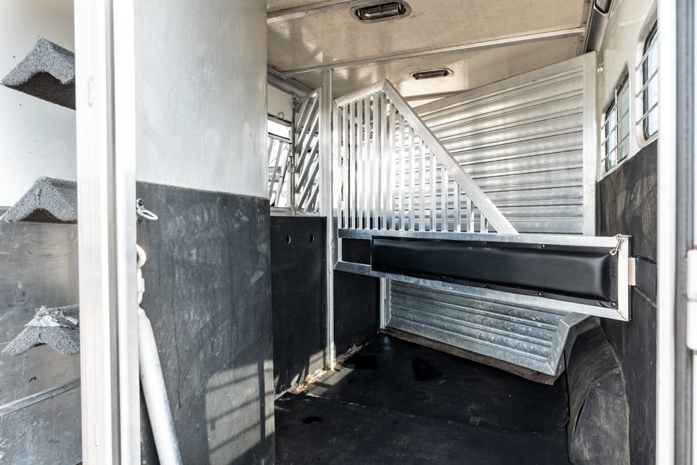 Interior of an empty horse trailer with a metal divider and aluminum walls