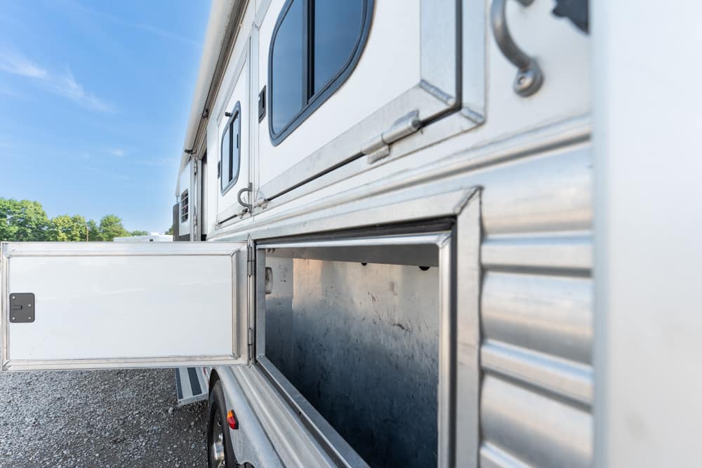 Open storage compartment on the side of a silver aluminum trailer, revealing an empty metal interior under a door frame.